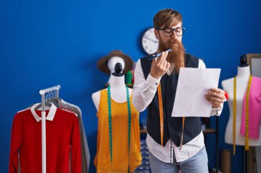 Genç kızıl saçlı terzi elbise fabrikasında akıllı telefon okuyarak konuşuyor.