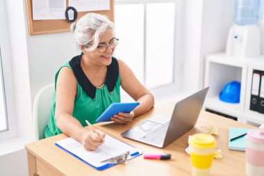 Orta yaşlı, kır saçlı iş kadını ofisteki dokunmatik kâğıdı kullanarak belgeye yazı yazıyor.