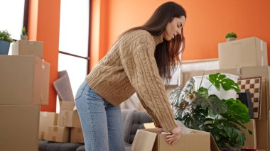 Young beautiful hispanic woman holding package at new home