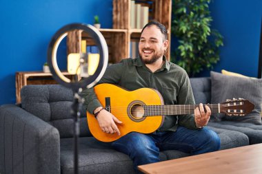 Ayrıca müzik stüdyosunda klasik gitar çalan, sakallı İspanyol bir adam kendini olumlu ve mutlu göstererek dişlerini gösteren bir gülümsemeyle ayakta duruyor. 