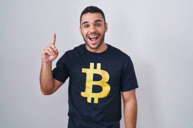 Bitcoin tişörtü giyen genç İspanyol adam başarılı bir fikri işaret ediyor. Heyecanlı ve mutlu. Bir numara.. 