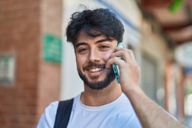 Sırt çantası takan genç bir İspanyol sokakta akıllı telefondan konuşuyor.