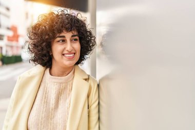 Orta Doğulu genç kadın güler yüzlü, kendinden emin bir şekilde caddenin kenarına bakıyor.