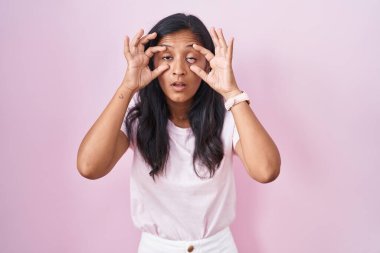 Pembe arka planda duran genç İspanyol kadın parmaklarıyla gözlerini açmaya çalışıyor, uykulu ve yorgun bir şekilde sabah yorgunluğu çekiyor. 