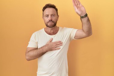 Sarı arka planda sakallı, elleri göğsünde, elleri açık yemin eden, sadakat yemini eden orta yaşlı bir adam. 