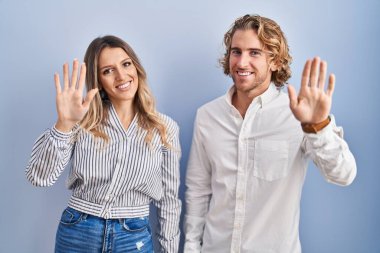 Mavi arka planda duran genç çift merhaba diyor mutlu ve gülümsüyor, dostça karşılama jesti 