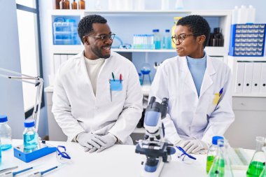 Erkek ve kadın bilim adamları laboratuvarda kendinden emin gülümsüyor.