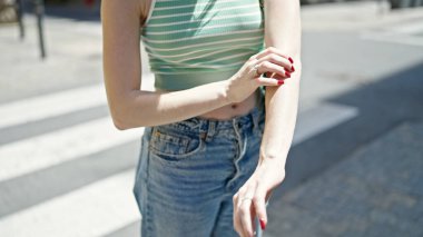 Sokakta kollarını tırmalayan genç sarışın kadın.