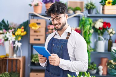 Young hispanic man florist smiling confident using touchpad at florist shop