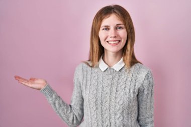 Güzel bir kadın pembe arka planda durup gülümseyerek sunar ve avuç içiyle kameraya bakar.. 