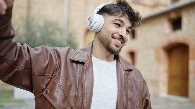 Genç Arap adam kendinden emin bir şekilde gülümsüyor müzik dinliyor ve sokakta dans ediyor.