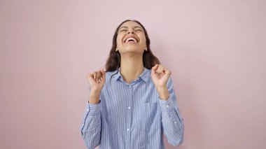 Soyutlanmış pembe arka planda kazanan yüz ifadesiyle duran genç, güzel İspanyol kadın.