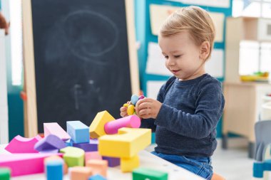 Anaokulundaki masada oturan sevimli sarışın çocuk geometri bloklarıyla oynuyor.
