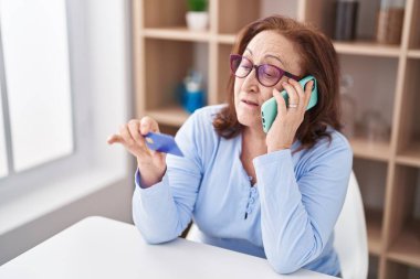 Üst düzey kadın akıllı telefondan konuşuyor ve evde kredi kartı kullanıyor.