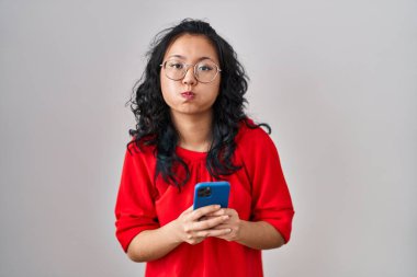 Genç Asyalı kadın akıllı telefon kullanıyor. Komik suratlı, yanak şişiren mesajlar yazıyor. Ağzı havayla şişer, havayı yakalar.. 