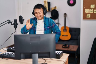 Çevrimiçi müzik dersine bakan genç Çinli adam pozitif ve mutlu görünüyor. Kendine güvenen bir gülümsemeyle ayakta duruyor ve dişlerini gösteriyor. 