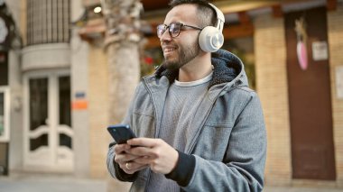 Hispanik adam güler kendine güvenen sokak telefonuyla müzik dinleyen