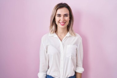 Pembe arka planda mutlu ve havalı bir gülümsemeyle duran genç ve güzel bir kadın. şanslı kişi. 