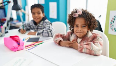 Sevimli afro-amerikan erkek ve kız öğrenciler masada oturmuş, kendilerine güvenerek gülümsüyorlar.