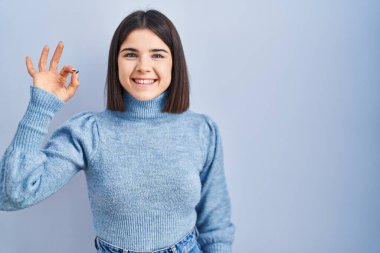 Mavi arka planda duran genç İspanyol kadın gülümsüyor ve el ve parmaklarıyla 