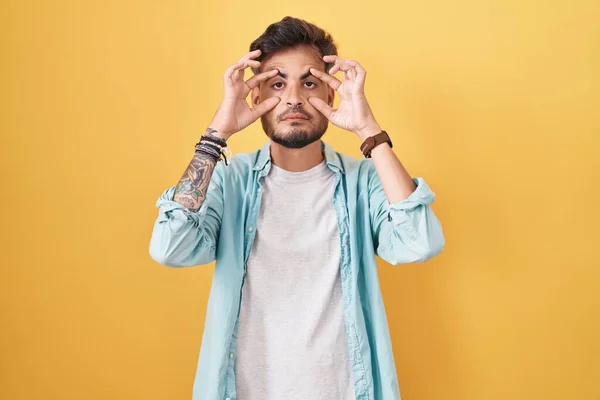 Jovem Hispânico Com Tatuagens Sobre Fundo Amarelo Tentando Abrir Olhos — Fotografia de Stock
