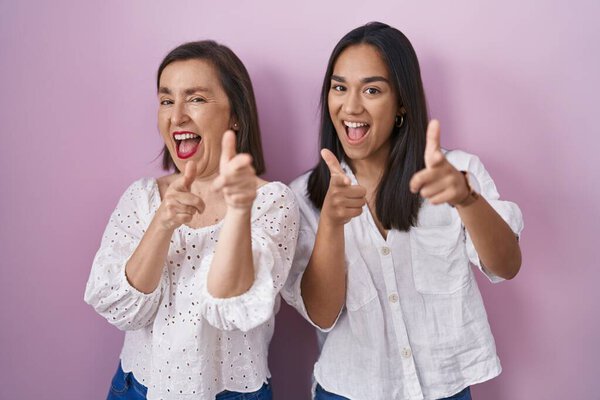 Hispanic mother and daughter together pointing fingers to camera with happy and funny face. good energy and vibes. 