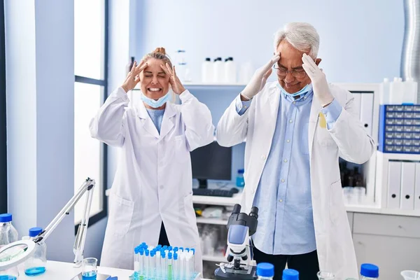 中年恐慌的人们手牵着手在实验室工作 头疼是因为压力 偏头痛 — 图库照片