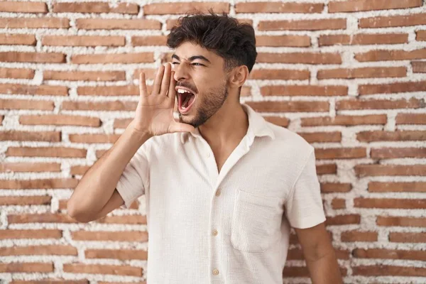 髭を生やしたアラブ人男性がレンガの壁の背景に大声で叫び 口の中で手で横に大声で叫んで立っている コミュニケーションの概念 — ストック写真