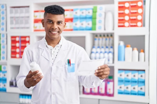年轻的拉丁裔男子药剂师在药店拿着药瓶看药方 — 图库照片