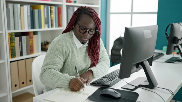 大学図書館のノートにコンピュータライティングを使用して編組髪の学生を持つアフリカの女性 — ストック写真