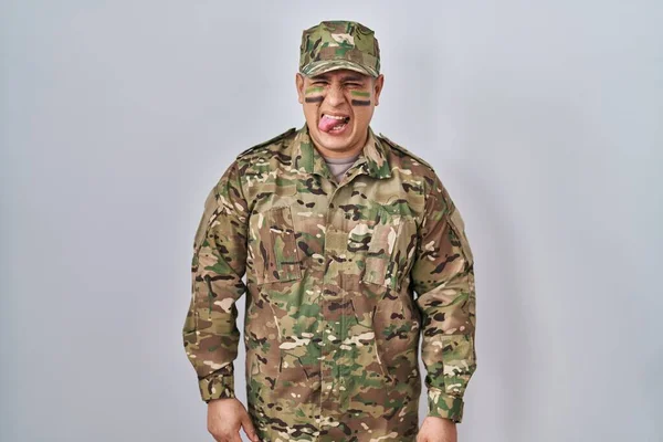Hispanic Young Man Wearing Camouflage Army Uniform Sticking Tongue Out — Zdjęcie stockowe