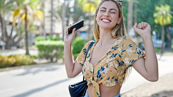 Молодая Блондинка Использует Смартфон Выражением Победителя Улице — стоковое фото