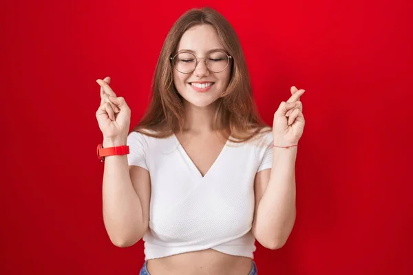 Młoda Kaukaska Kobieta Stojąca Nad Czerwonym Tłem Trzymająca Kciuki Uśmiechnięta — Zdjęcie stockowe
