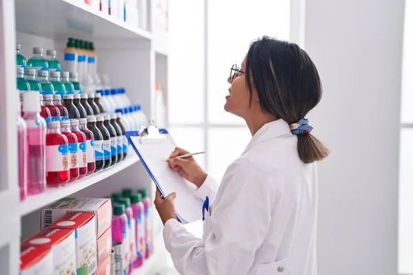 Young Hispanic Woman Pharmacist Writing Document Looking Shelving Pharmacy — 图库照片