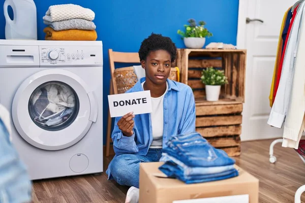 African american woman donating clothes thinking attitude and sober expression looking self confident