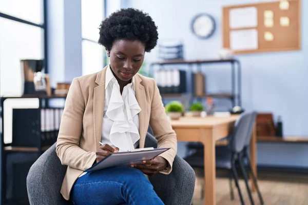 若いアフリカ系アメリカ人女性のビジネスワーカーがオフィスで椅子に座って書類作成に書きます — ストック写真