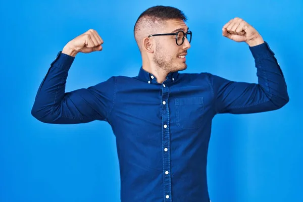 Mavi Arka Planda Gözlük Takan Spanyol Genç Adam Gururla Gülümseyen — Stok fotoğraf