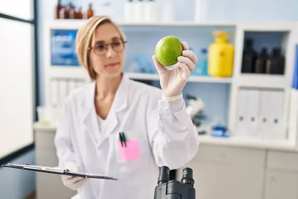 Young Blonde Woman Scientist Holding Apple Reading Report Laboratory — Stock fotografie