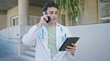 Genç İspanyol doktor hastanede dokunmatik ped kullanarak akıllı telefondan konuşuyor.