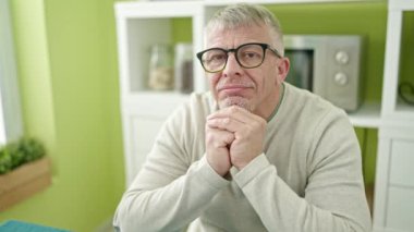 Middle age grey-haired man smiling confident sitting on table at home