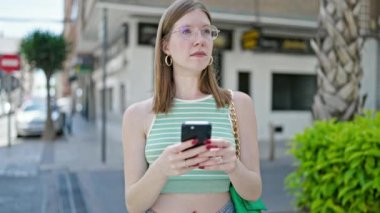 Akıllı telefon kullanan genç sarışın kadın varış noktasını caddede arıyor.