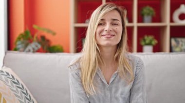 Sarışın genç bir kadın evdeki koltukta kendinden emin bir şekilde oturarak gülümsüyor.