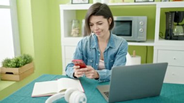 Evde akıllı telefon ve dizüstü bilgisayar kullanan beyaz bir kadın.