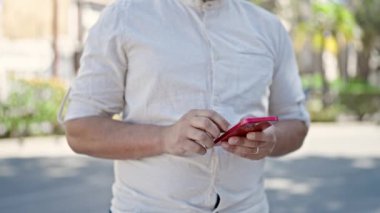 Young hispanic man using smartphone at park