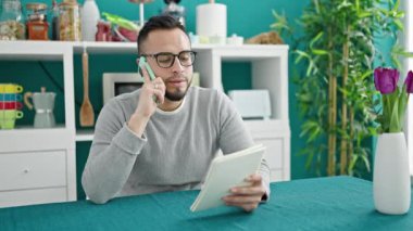 İspanyol adam yemek odasında telefon okuyarak konuşuyor.