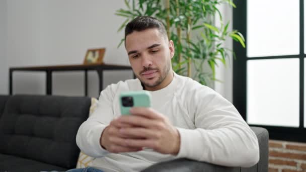 Νεαρός Ισπανόφωνος Άντρας Που Χρησιμοποιεί Smartphone Κάθεται Στον Καναπέ Στο — Αρχείο Βίντεο