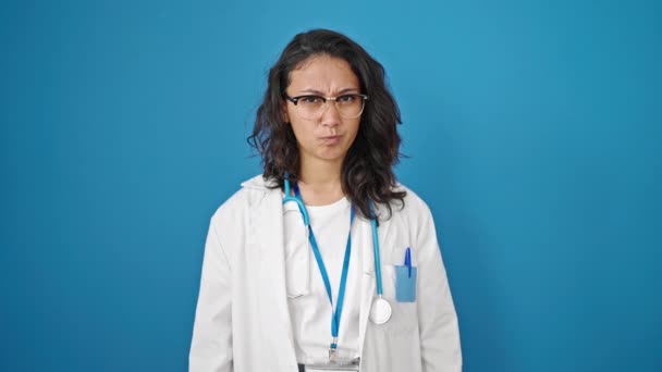 若いです美しいですヒスパニック女性医師怒りと強調上の隔離された青い壁の背景 — ストック動画