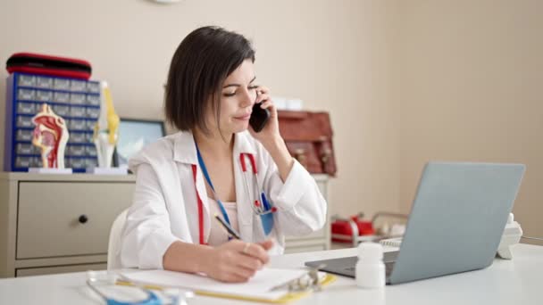 Νεαρή Καυκάσια Γιατρός Μιλάει Στο Τηλέφωνο Γράφοντας Έγγραφο Στην Κλινική — Αρχείο Βίντεο