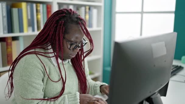 大学図書館で首の痛みを持つコンピュータを使用して編組髪の学生を持つアフリカの女性 — ストック動画