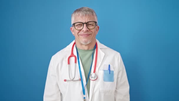 中年白发男子医生在孤立的蓝色背景下竖起大拇指 — 图库视频影像